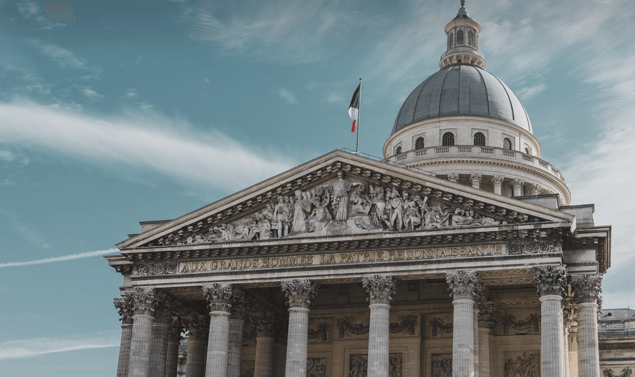 The Pantheon in Paris, with a French flag atop its dome, under a blue sky with wispy clouds.