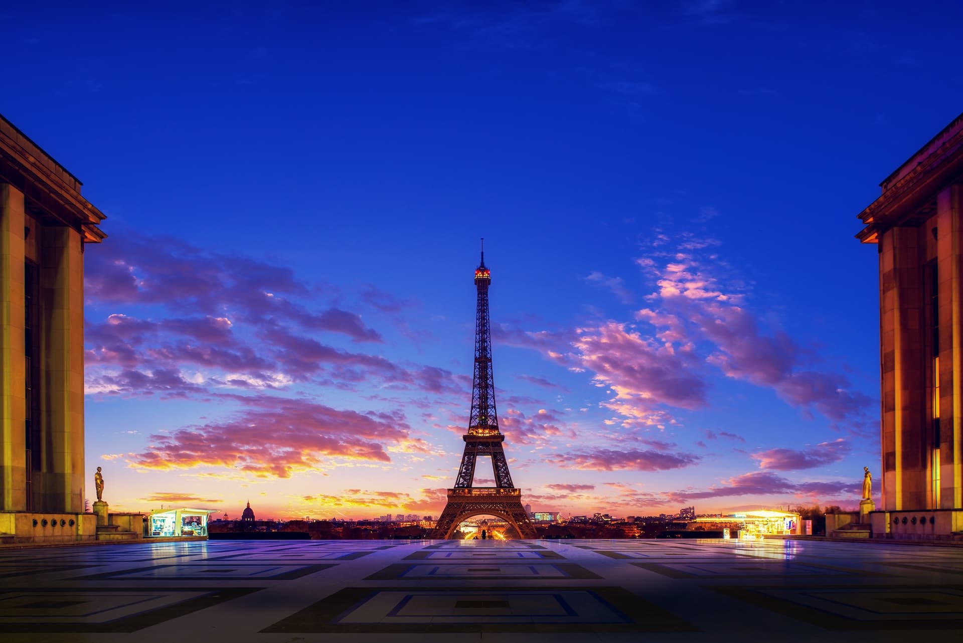 Eiffel Tower at sunset, framed by two buildings, with a vibrant sky of purple and orange clouds.